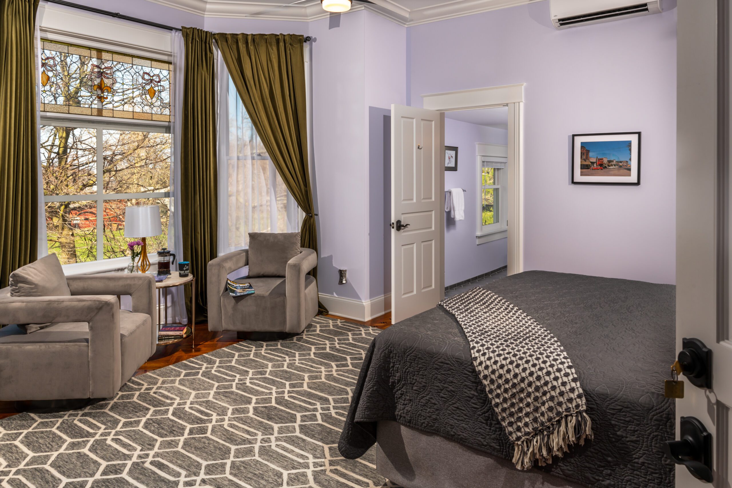 Port_Austin_Bed_and_Breakfast_Port_Austin_Hotel_Room 3-01_Md - Port Austin Bed & Breakfast Image of King bed with gray bedspread and room with large picture windows and seated chairs.