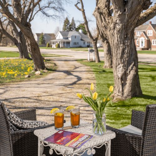 Port_Austin_Bed_and_breakfast_Port_Austin_Hotel_Patio - Port Austin Bed & Breakfast 2 glasses of ice tea and tulips on a table near chairs on a porch