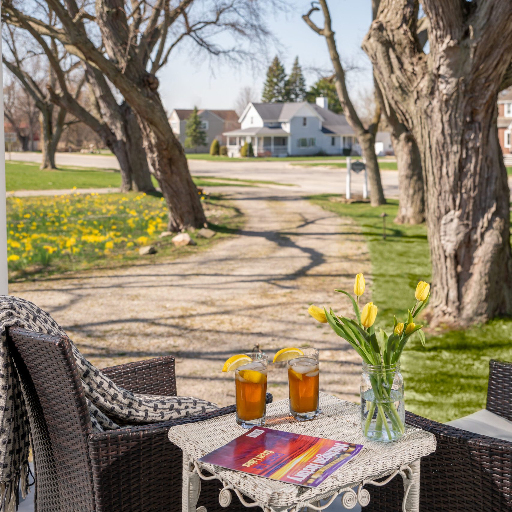 Front Porch-01_Md - Port Austin Bed & Breakfast Image of two chairs with table with iced tea and yellow tulips on front porch