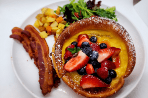 Port_Austin_Bed_and_Breakfast_Port_Austin_Michigan_Hotel_Image 12 - Port Austin Bed & Breakfast Berry Dutch Baby pancake, bacon, potatoes and salad on a plate