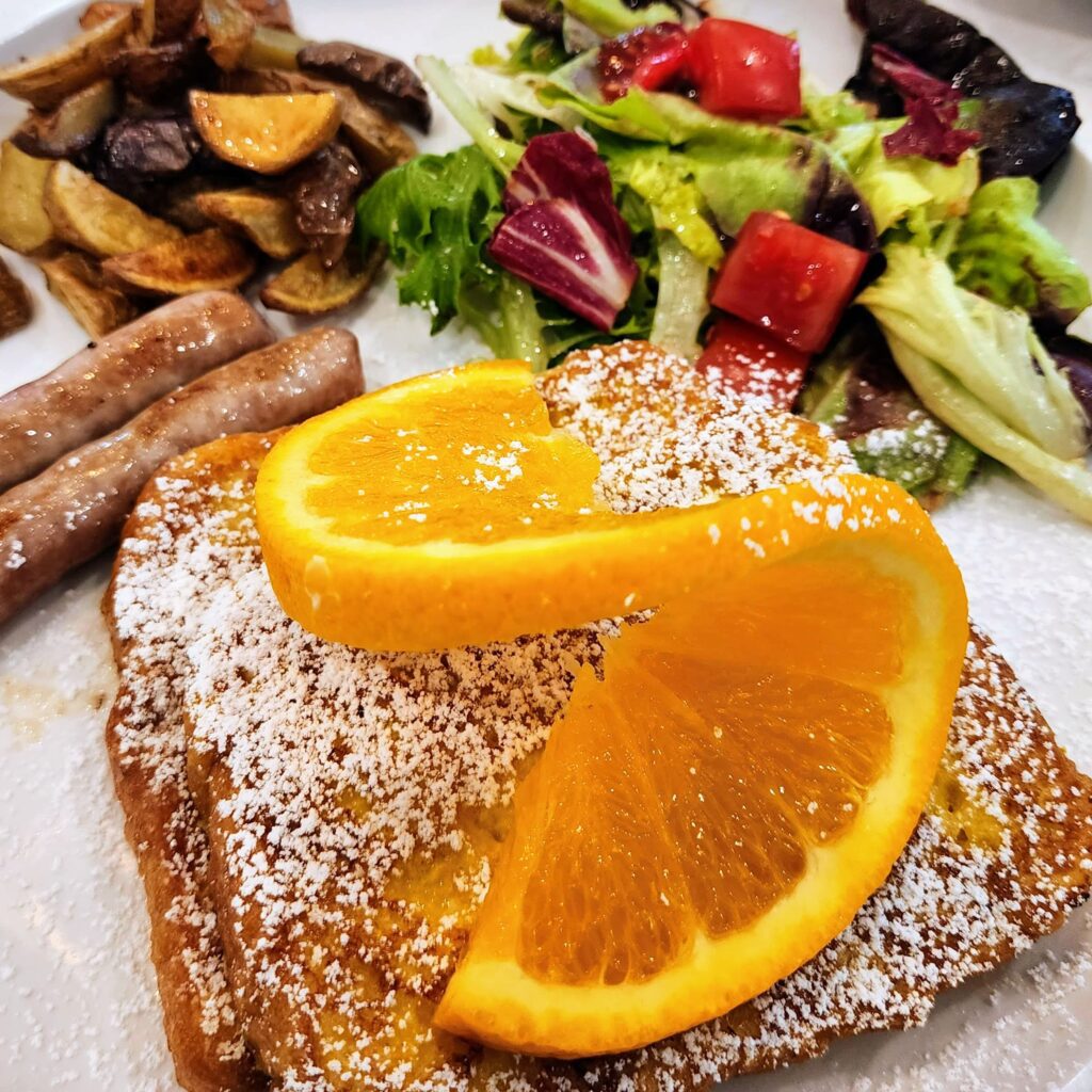 French Toast topped with a slice of orange, sausage, potatoes and salad